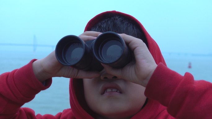 小男孩在游船上用双筒望远镜观看时感到惊讶