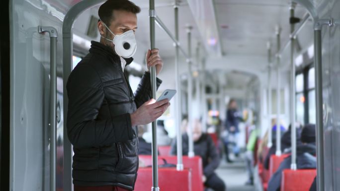 乘坐有轨电车的男子戴着防护面罩使用手机
