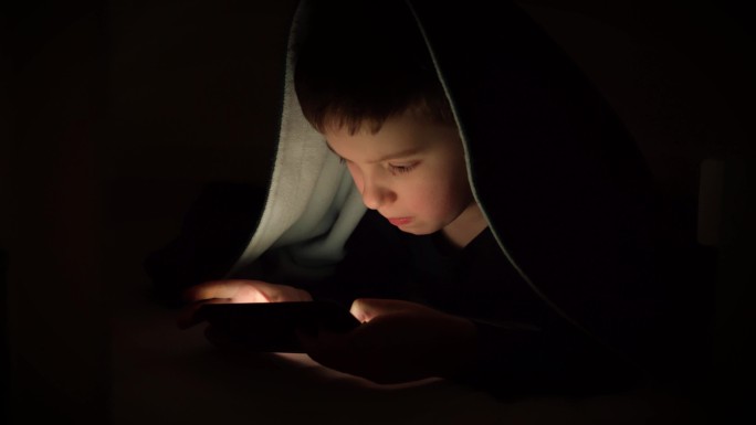 小男孩在毯子下玩手机