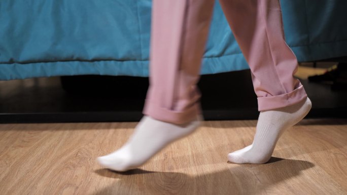 穿着白色袜子和粉色裤子的女人偷偷地从卧室地板上走过