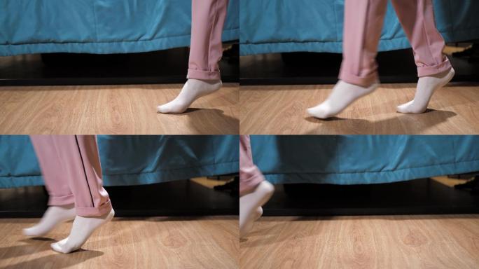 穿着白色袜子和粉色裤子的女人偷偷地从卧室地板上走过