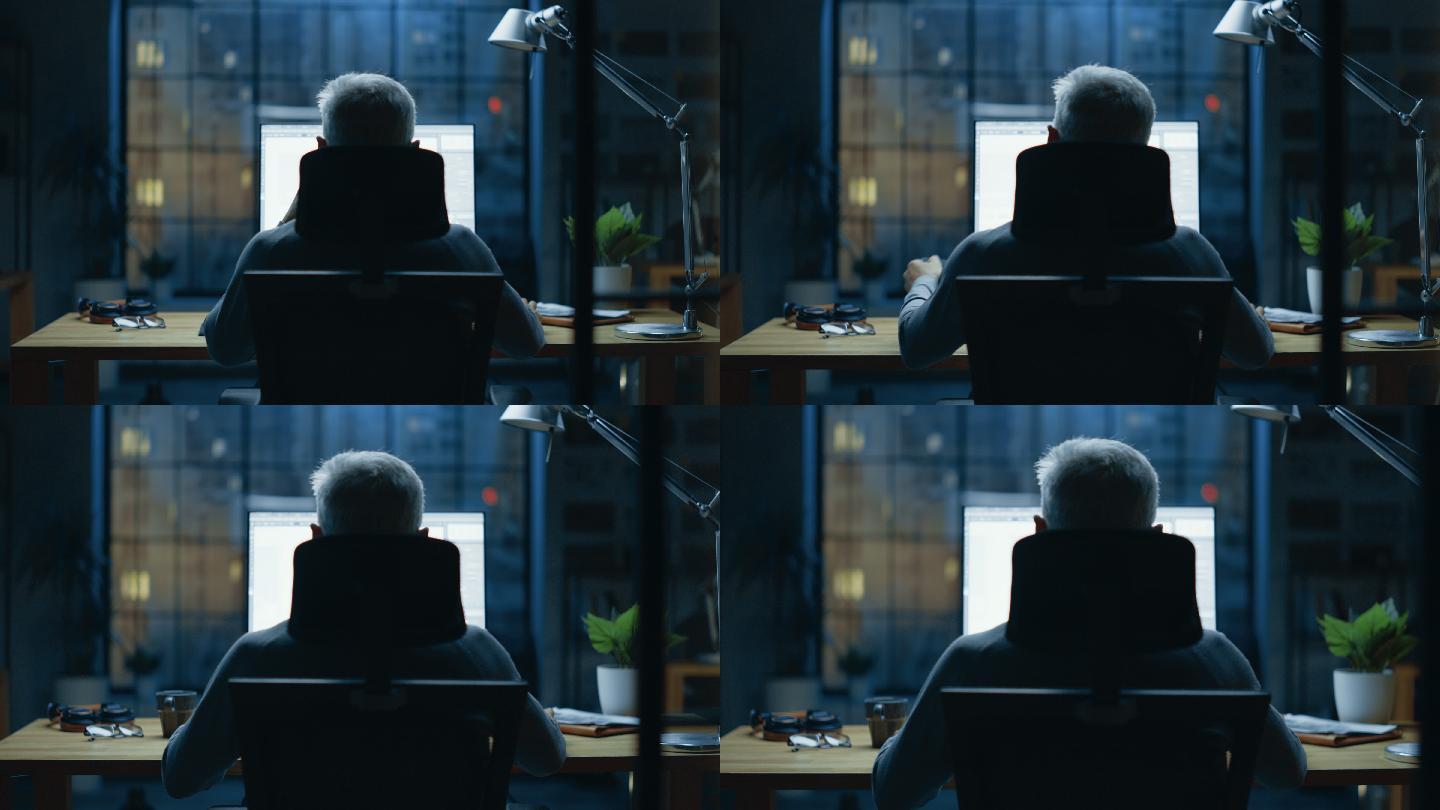 商人坐在桌旁使用台式电脑的后视图。