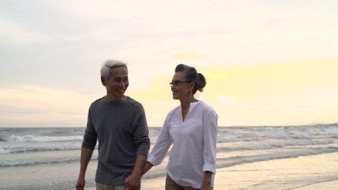 老年夫妇牵手漫步在日落海滩上