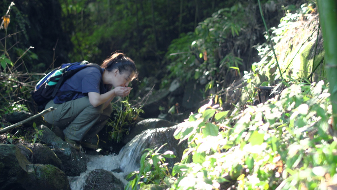 背包客美女山间小溪双手捧水喝山泉水