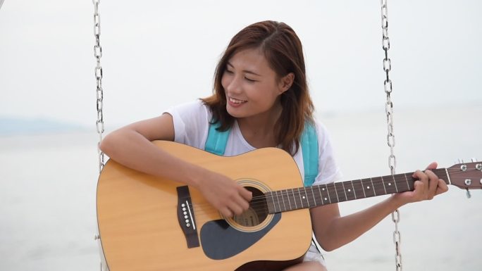 美丽的女孩在海滩上弹原声吉他。