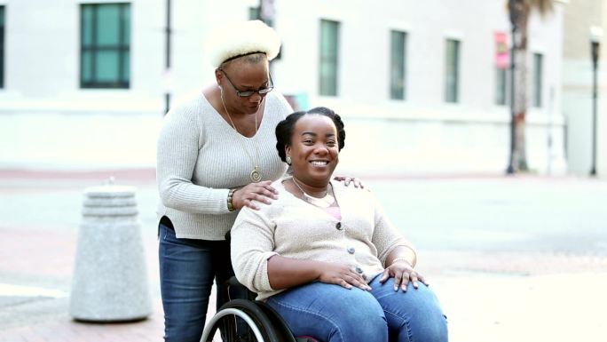 坐轮椅的妇女和年长的母亲在城市街道上