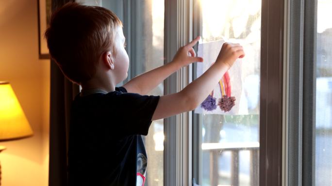 新冠疫情期间，一个小男孩在家窗户上贴画