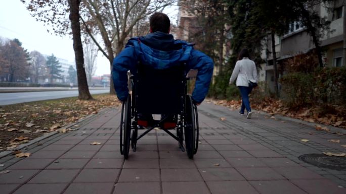 坐轮椅沿着人行道的年轻人