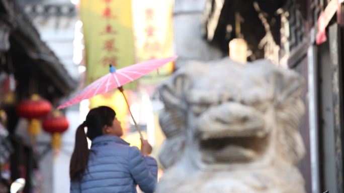 古巷里女孩撑伞走过石狮子雕塑