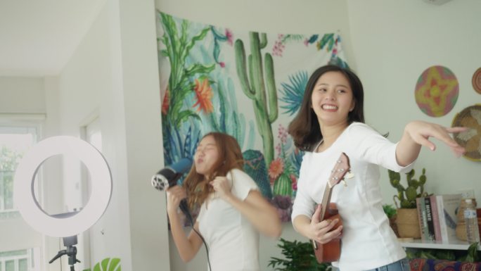 两个女孩在卧室里用吹风机跳舞唱歌弹吉他。