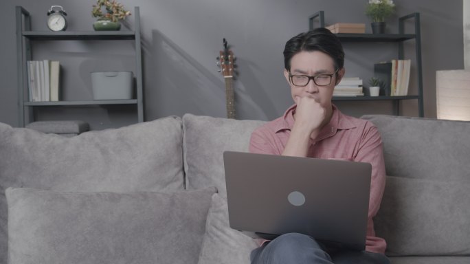 男子坐在家客厅的沙发上，用笔记本电脑阅读