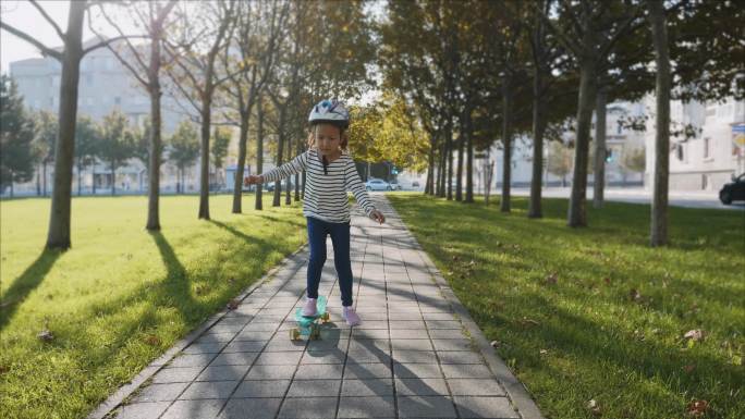 小女孩戴着防护头盔慢慢地在滑板