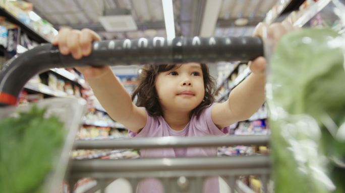 一个小女孩在超市里快乐地推着购物车