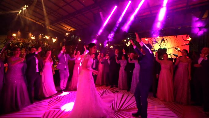 新婚夫妇翩翩起舞，而婚礼宾客则挥舞手臂