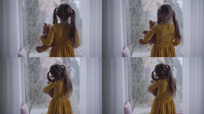 小女孩抱着泰迪熊望着窗外的后视图。