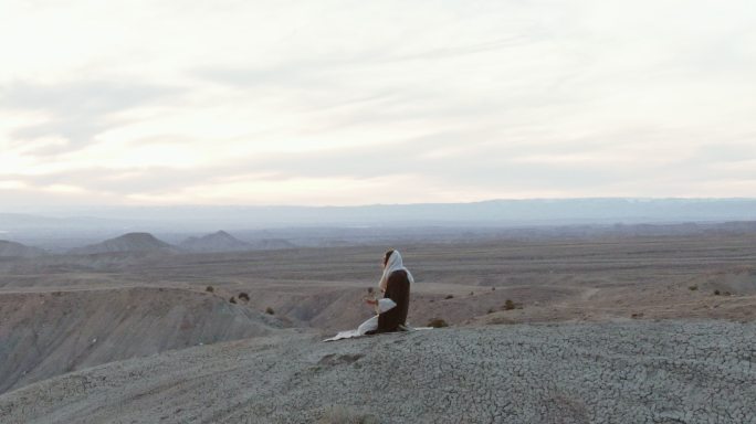 在日出，耶稣基督跪在沙漠山坡上祈祷