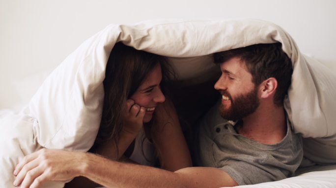 一对幸福的年轻夫妇在家用毯子盖住自己