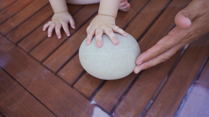 婴儿和他的爷爷正在玩一块大石头。