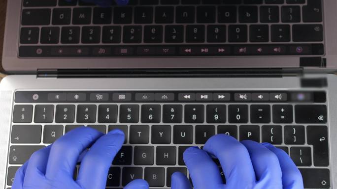 医生戴着蓝色外科手套在笔记本电脑上打字