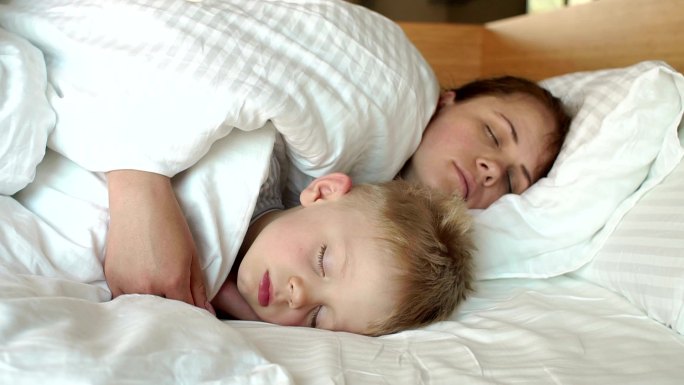 母亲和孩子早上一起睡在白色的床上