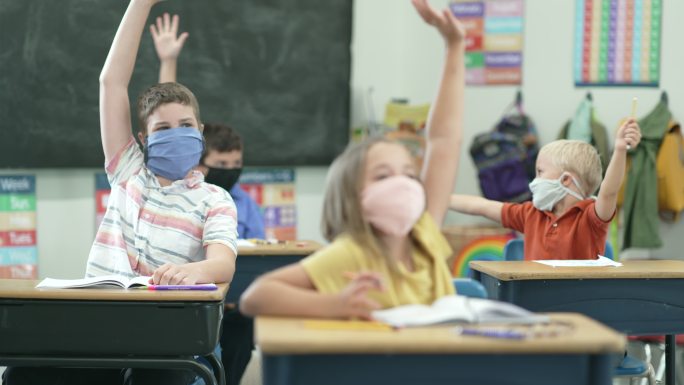 小学生在教室里戴着防护口罩举手回答问题