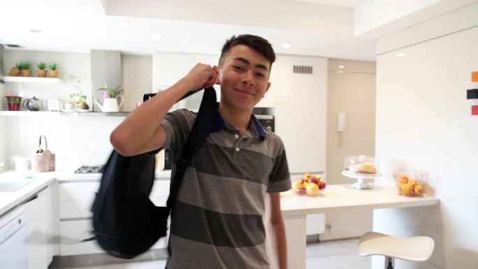 一个十几岁的小男孩在厨房里捡起他的书包