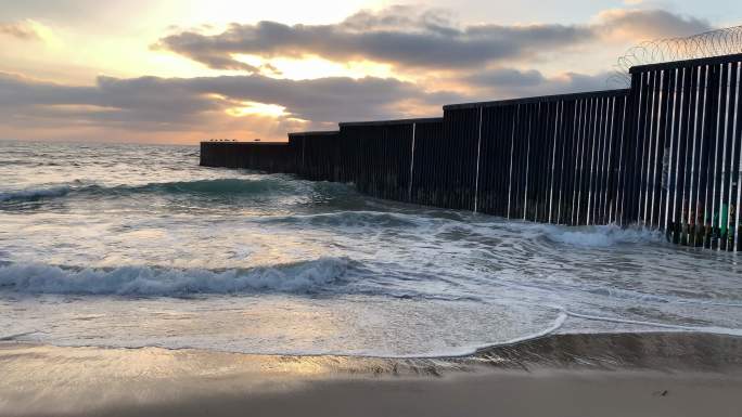 国际边界墙附近日落时的海滩和海浪