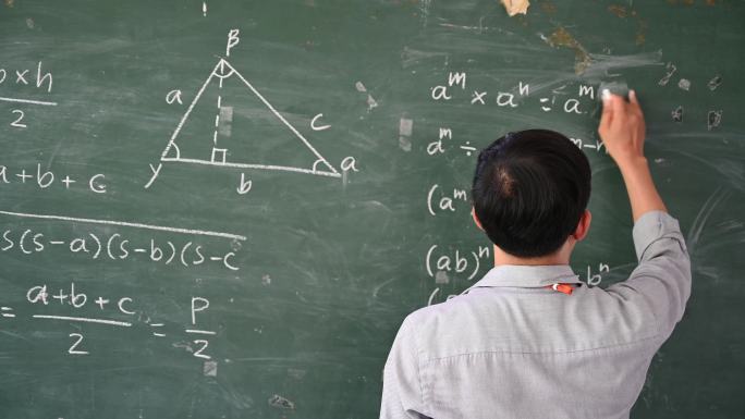 男老师在课堂上用白色粉笔在黑板上写字