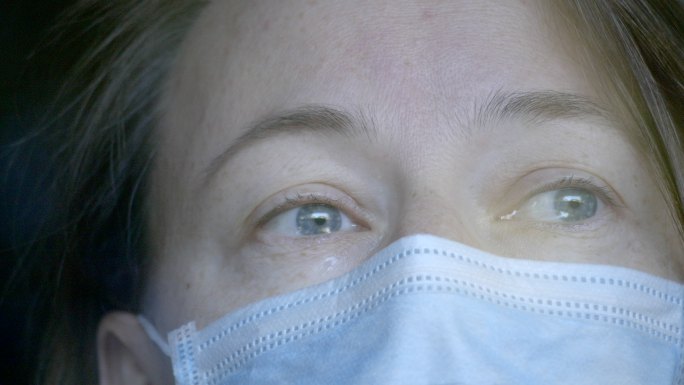 戴着医用口罩的女人透过窗户哭泣。