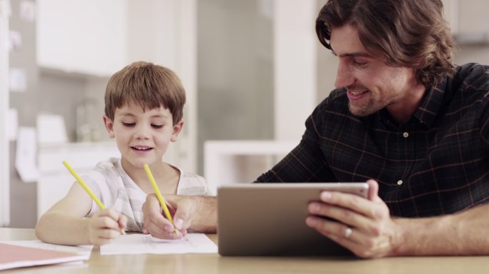 一位父亲拿着一台平板电脑帮助儿子完成学业