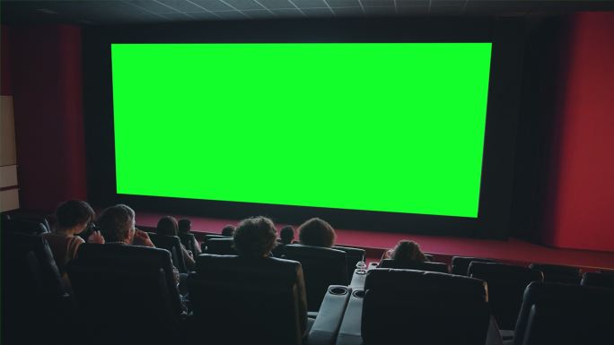 人们在电影院看大绿色屏幕欣赏电影