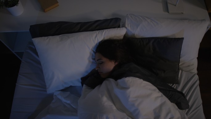 俯视图：年轻女子晚上睡觉时在床上翻身