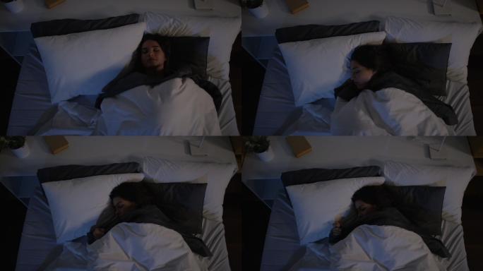 俯视图：年轻女子晚上睡觉时在床上翻身