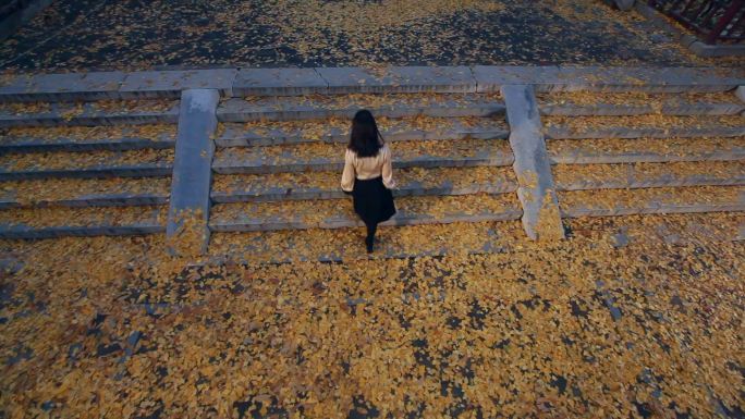 女孩走在落满银杏树叶的台阶上