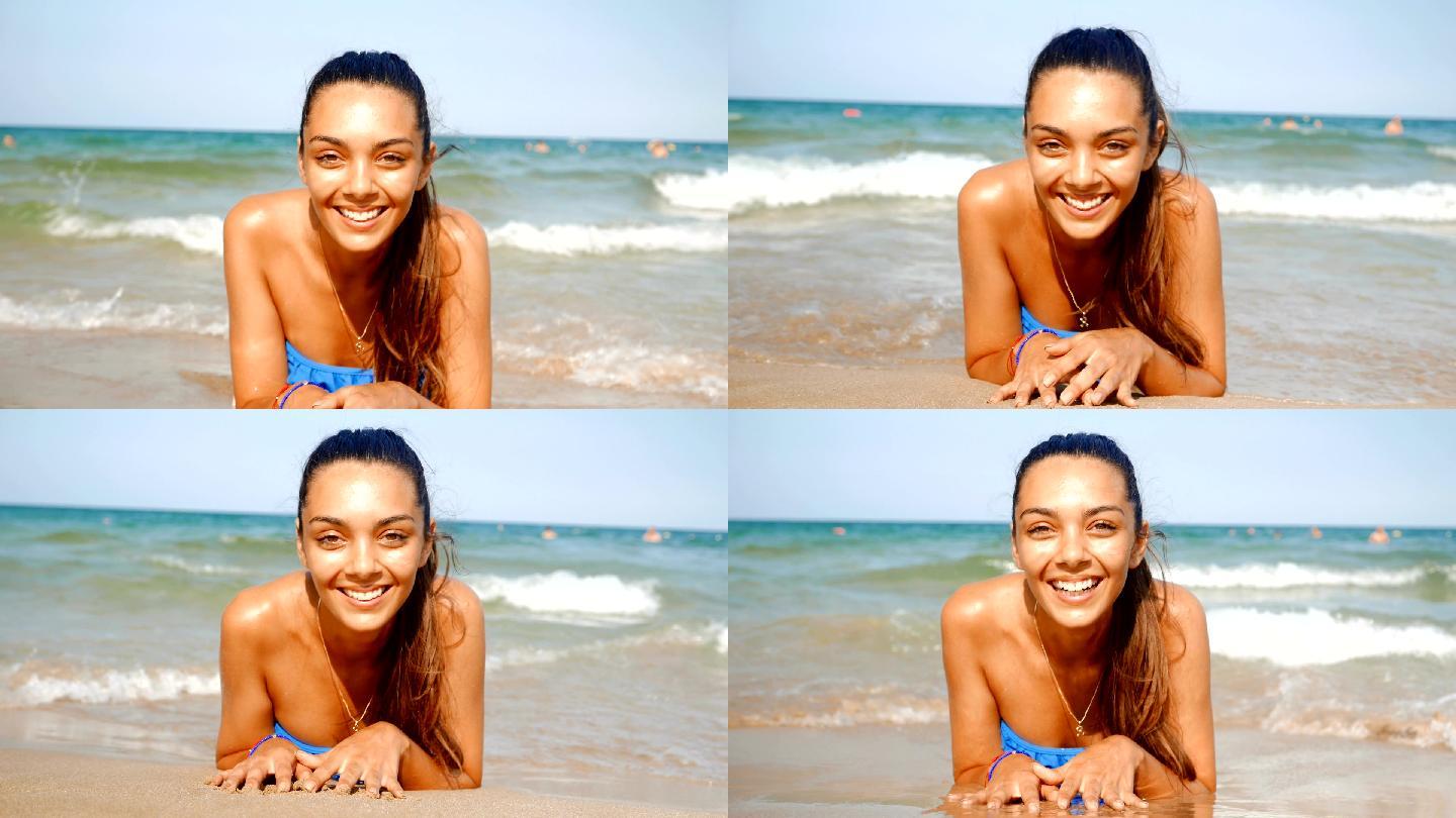 海滩上美丽的年轻女子躺在水里看着相机