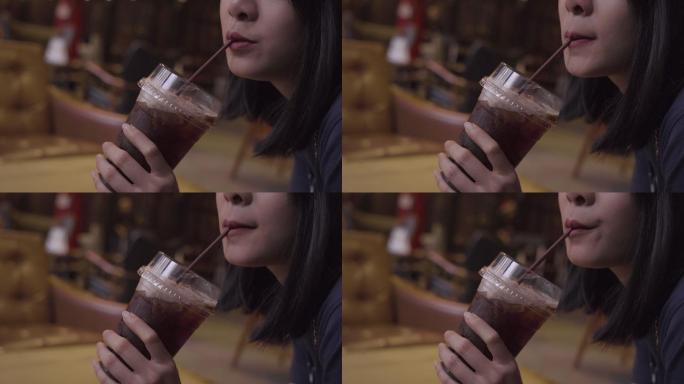 年轻女孩在咖啡馆用吸管喝咖啡。