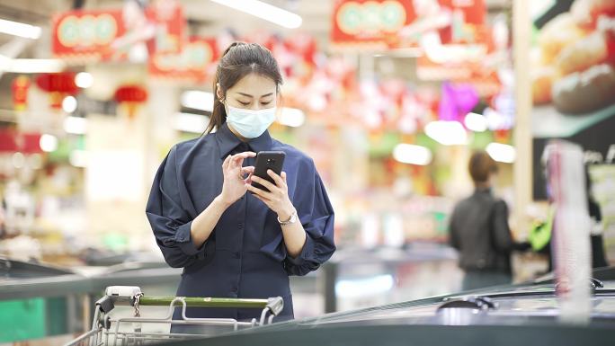 年轻中国女性拿着手机逛超市