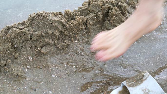 一个人在海边沙滩上堆沙堆，堆砌沙雕水坝