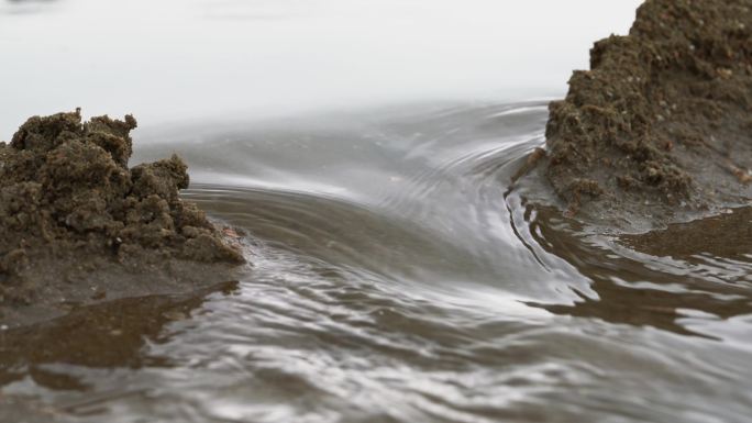 一个人在海边沙滩上堆沙堆，堆砌沙雕水坝