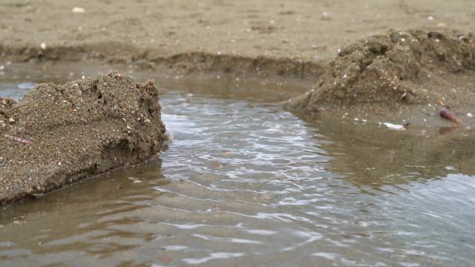 一个人在海边沙滩上堆沙堆，堆砌沙雕水坝