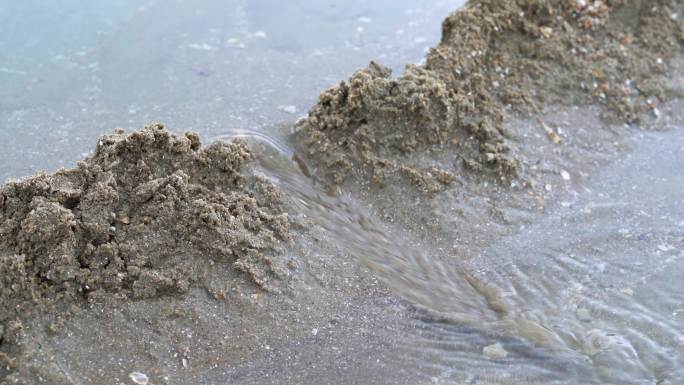 一个人在海边沙滩上堆沙堆，堆砌沙雕水坝