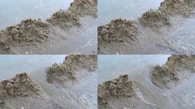 一个人在海边沙滩上堆沙堆，堆砌沙雕水坝
