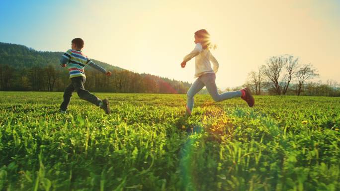 男孩和女孩在阳光明媚的草地上奔跑