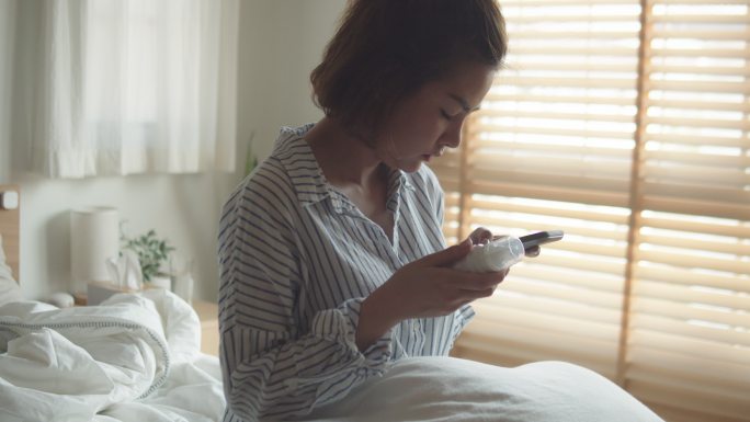 在卧室里拿着药瓶和手机聊天的女子