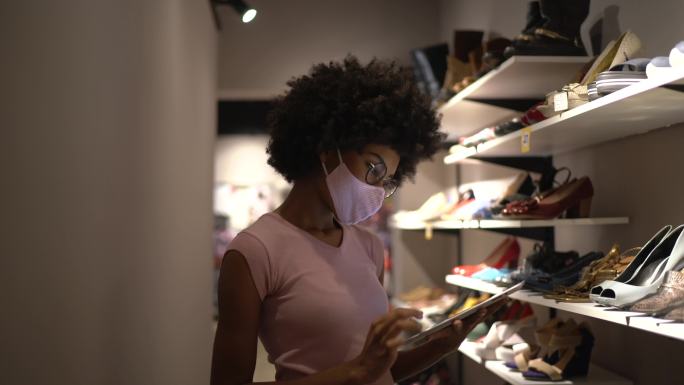 一位戴着口罩并使用电脑在鞋店工作的女性