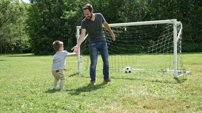年轻的父亲和小儿子在足球场上踢足球