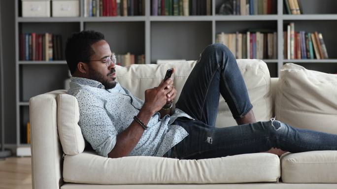 年轻的非洲小伙子在家里用手机在沙发上放松
