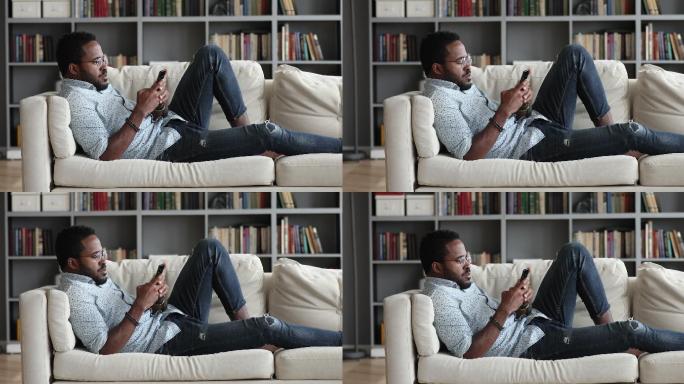 年轻的非洲小伙子在家里用手机在沙发上放松