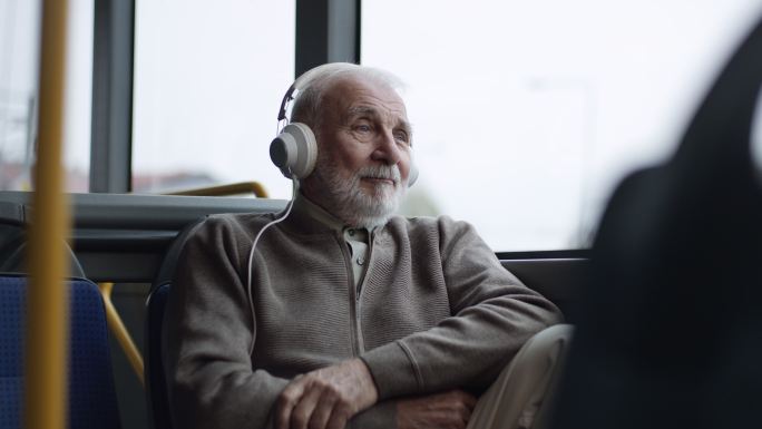 在公共汽车上用耳机听音乐的老人