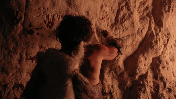 穿着兽皮的原始人在墙上画画。